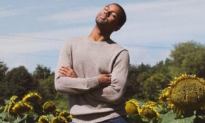 Byrd Barr Place's Director of Operations Tremayne Edwards standing in a field of sunflowers with his eyes closed and head titled toward the sun.