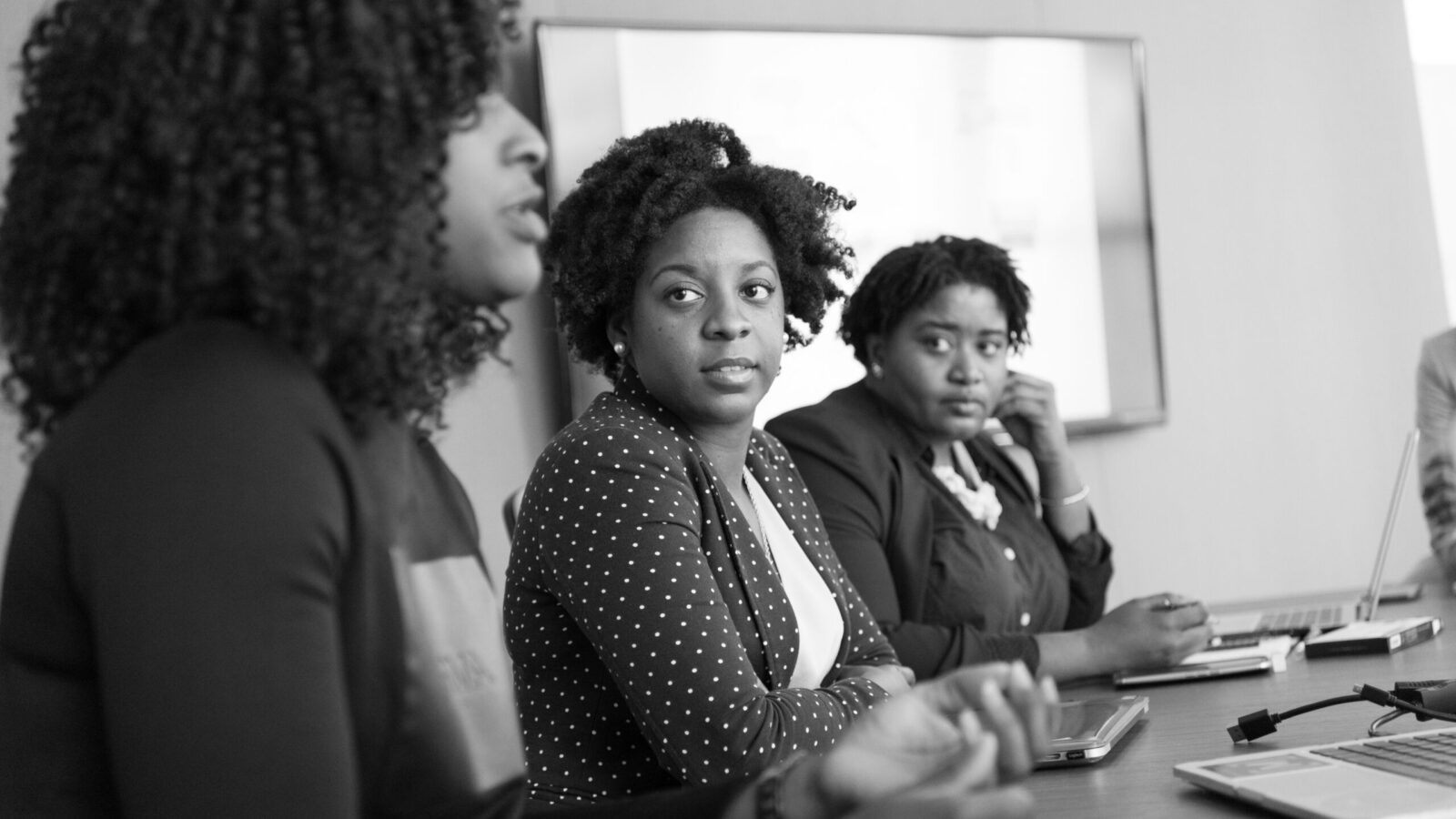 Three black women in a meeting room dressed in business clothes