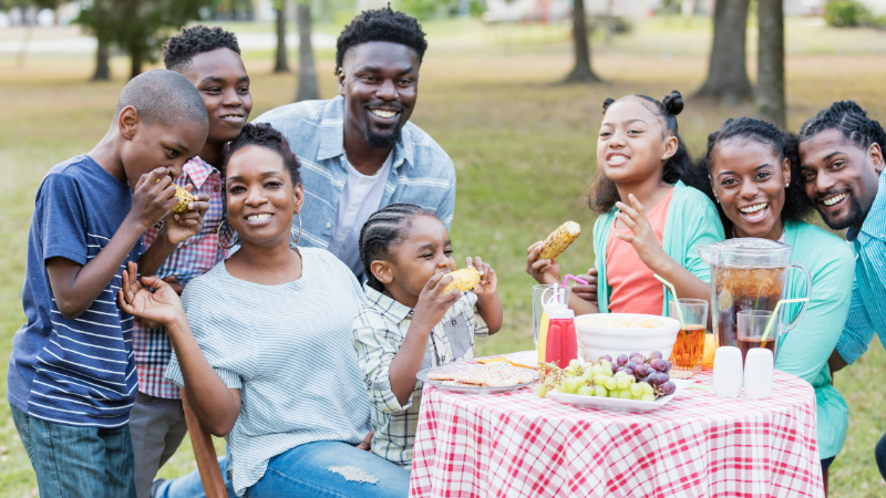 Black family having a lunch outdoors at a park with a small picnic table and snacks
