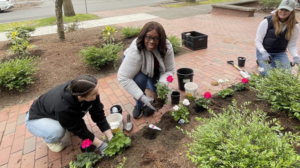 CEO Dr. Angela Griffin with two volunteers planting flowers in the front yard of Byrd Barr Place.