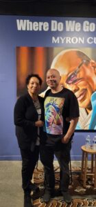 Two people smiling in front of a painting